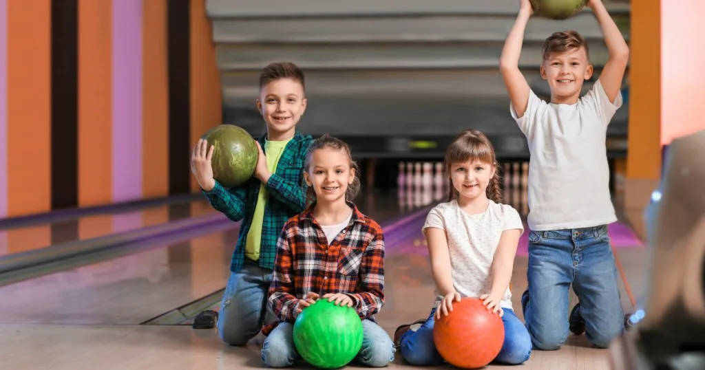 Kids bowl free ontario - 4 children holding bowling balls in the bowling alley in Ontario