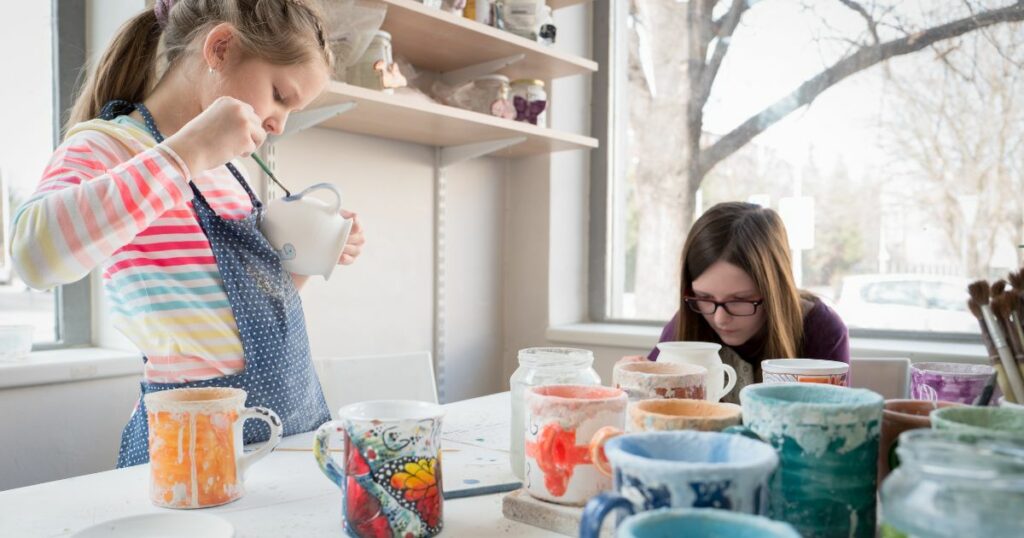 two girls painting pottery mugs in a pottery studio