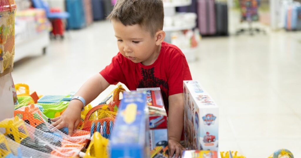 Little boy in a red shirt looking at toys at a toy store